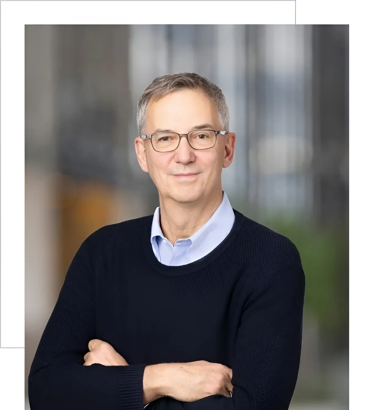 Portrait of a smiling middle-aged man wearing glasses and a dark sweater.